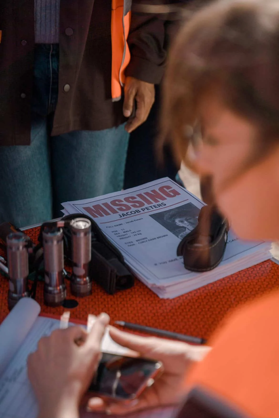 Detective agency investigation scene with missing person case files, flashlights, and investigators reviewing evidence during a search operation.